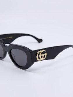 Svart, sofistikert solbrille med logo i gull på brillestenger
