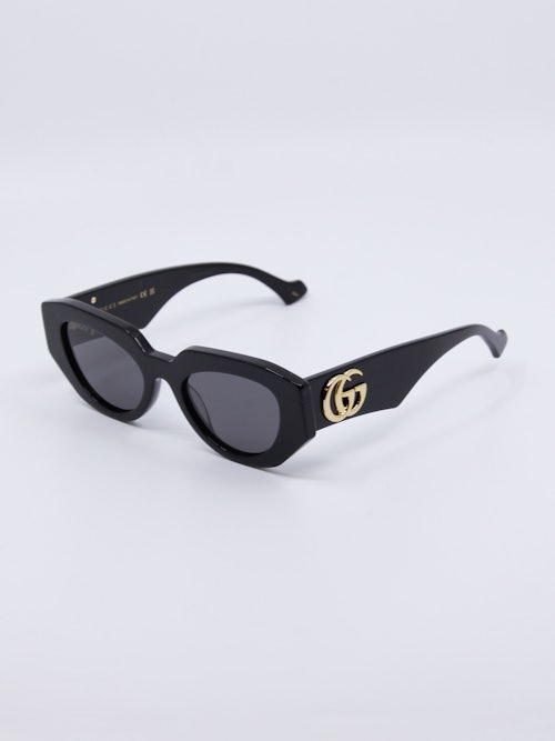Svart, sofistikert solbrille med logo i gull på brillestenger