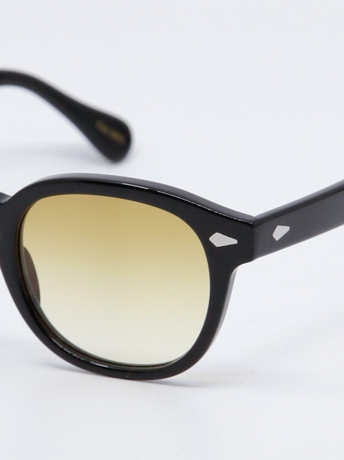 Rund solbrille med sort ramme og  karamell fargede, gradert glass, nærbilde