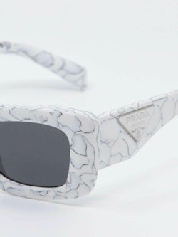 Hvit solbrille med marmordesign og svarte glass, nærbilde fra siden
