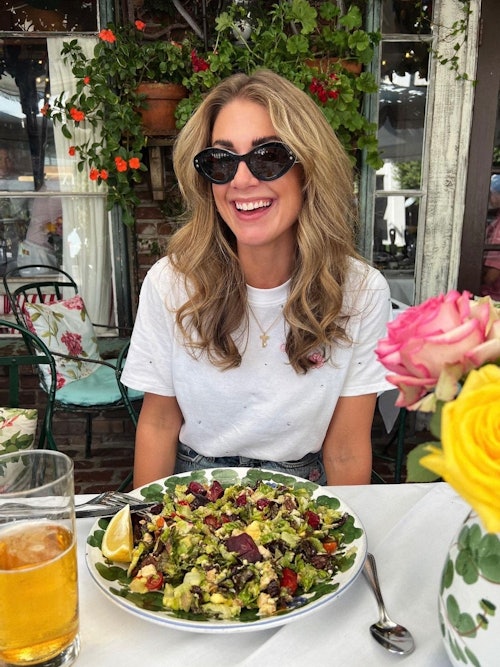 Jente smiler med solbriller ved et bord med mat