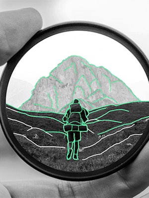 Illustrasjon av en linse som holdes i en hånd. I linsen ser man et fjell og en person som går tur.