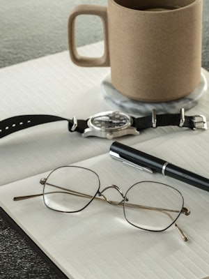 Bilde av en metallinnfatning fra Krogh Optikk som ligger på en bok sammen med klokke, penn og en kaffekopp.